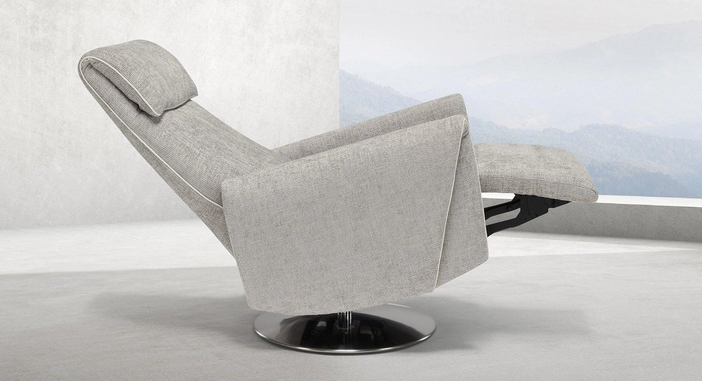 Der Relax- & Aufstehsessel Muna mit einer verstellbaren Rückenlehne und Fußstütze, positioniert in einer zurückgelehnten Haltung. Der Sessel steht auf einem runden Metallfuß in einem modernen, minimalistischen Raum mit hellen Wänden. Im Hintergrund erstreckt sich ein großes Panoramafenster mit Blick auf eine nebelverhangene Berglandschaft.