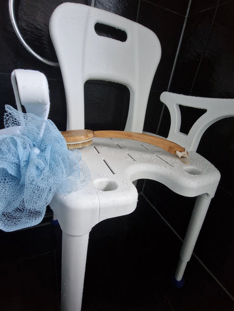 Duschstuhl AiO von Drive Medical in einer schwarzen Dusche, nass vom Gebrauch, mit blauer Duschblume und Badebürste auf der Sitzfläche – zeigt Alltagseinsatz und Hygieneausschnitt