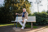 Älterer Mann sitzt auf einer Parkbank und stützt sich auf einen blauen Hurrycane Gehstock von Drive Medical – ideal für sicheres Gehen im Freien.