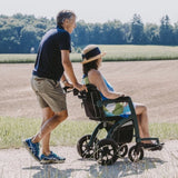 Paar spaziert durch ländliche Landschaft – Frau sitzt im Rollz Motion 2.1 Rollstuhl, der von ihrem Partner geschoben wird.